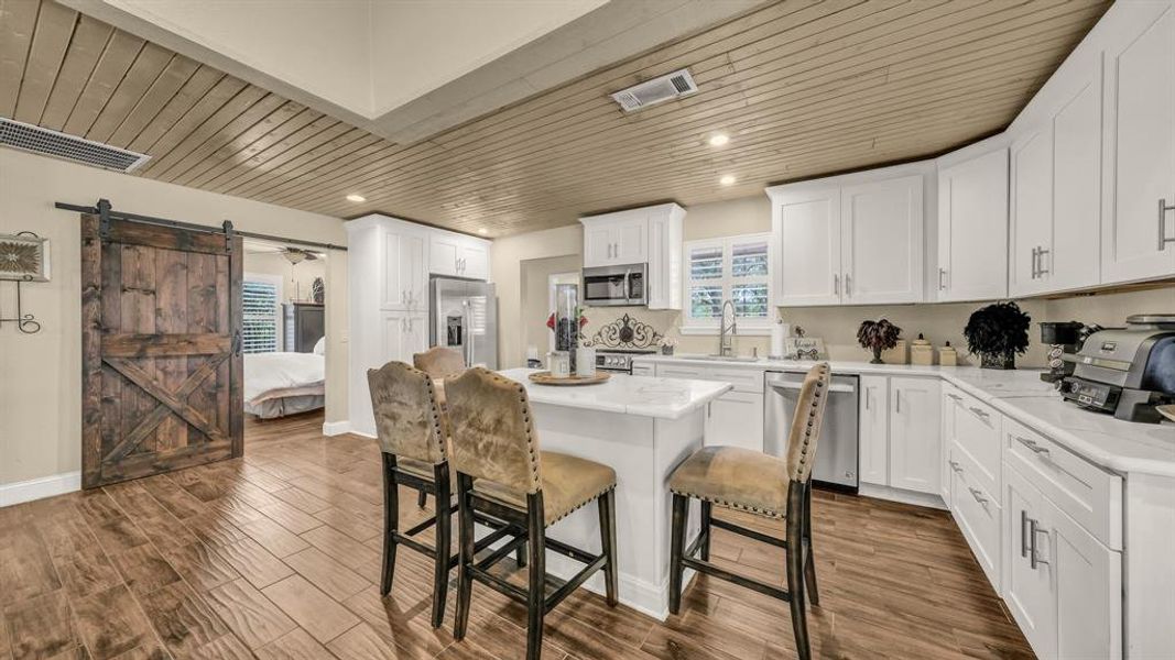 Kitchen with appliances with stainless steel finishes, a barn door, a center island, white cabinetry, and dark wood-type flooring