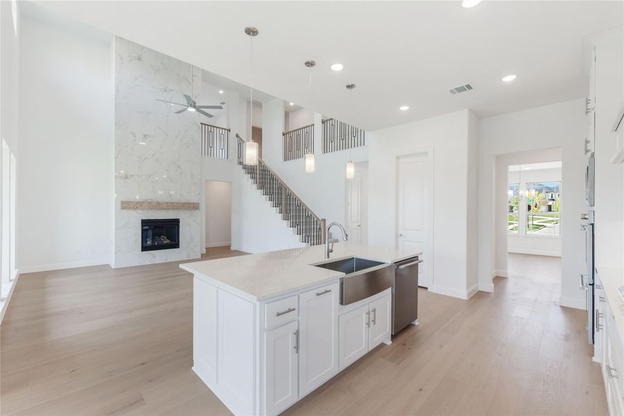 Open-concept kitchen with white island, farmhouse sink, and marble fireplace wall with staircase in background