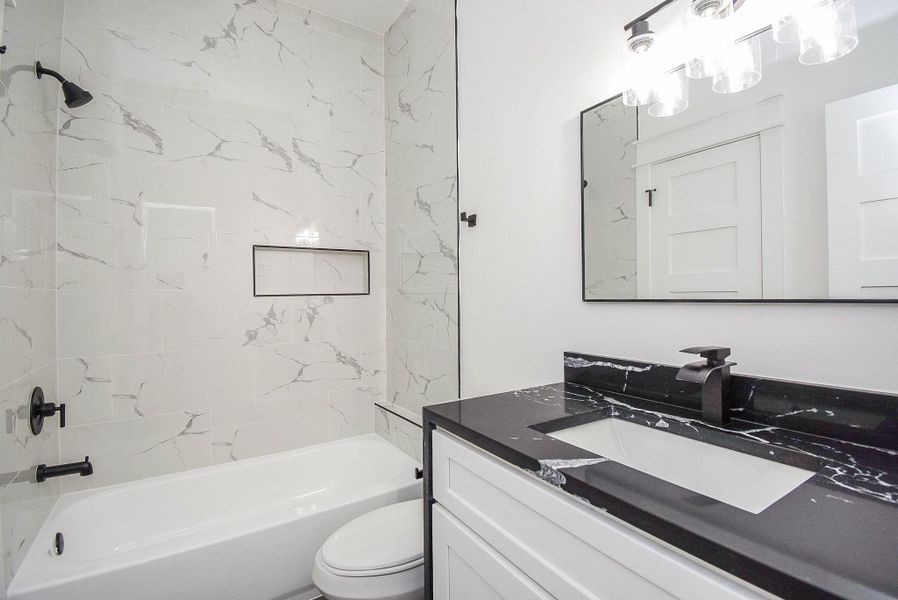 Modern bathroom with elegant marble tile, a sleek black countertop, and a stylish vanity. The bathtub features a built-in niche, and contemporary fixtures complete the clean, sophisticated look.