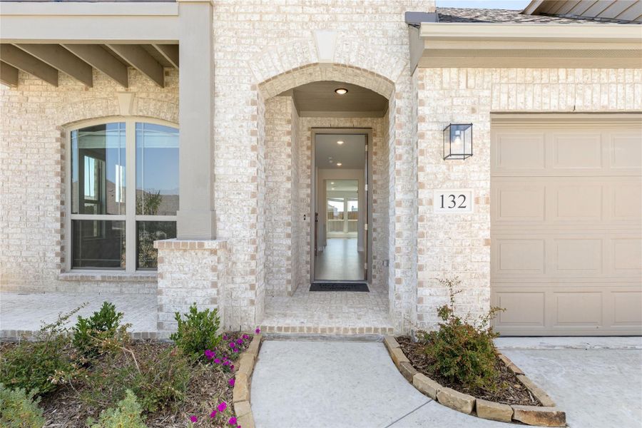 Home entrance with arched brick surround, glass front door, house number 132, and attached garage