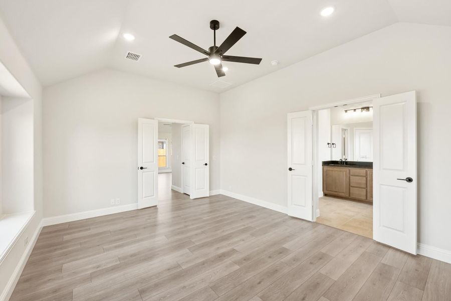 Empty master bedroom with vaulted ceiling, ceiling fan, hardwood floors, and open ensuite bathroom door Empty master bedroom with vaulted ceiling, ceiling fan, hardwood floors, and open ensuite bathroom door