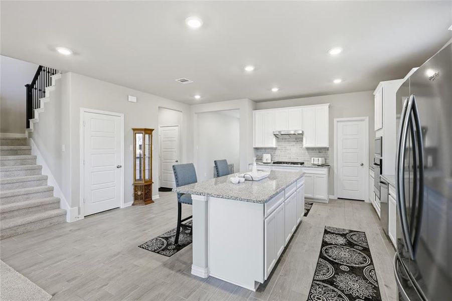 Modern kitchen featuring a central island with granite countertop, white cabinetry, stainless steel appliances, and tile backsplash