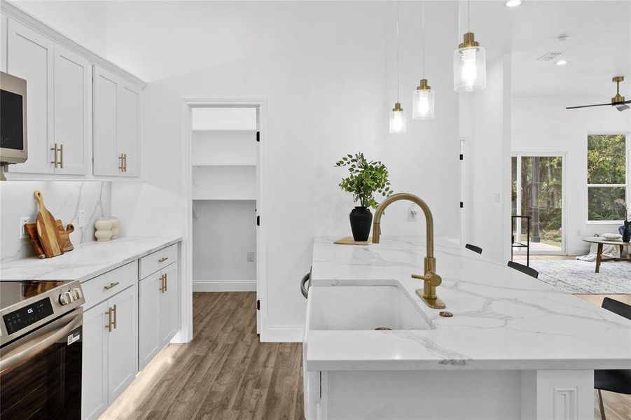 Kitchen featuring white cabinets, decorative light fixtures, stainless steel appliances, light stone countertops, and light wood finished floors Kitchen featuring white cabinets, decorative light fixtures, stainless steel appliances, light stone countertops, and light wood finished floors