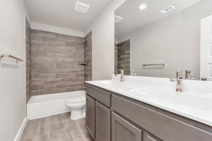 Indulge in refined charm in the secondary bathroom, where the tile flooring harmonizes with a bath/shower combo surrounded by tasteful tile. Dark wood cabinets, double sinks coupled with a gorgeous countertop, elevate the space, cultivating a truly welcoming atmosphere.  Sample photo of completed plan. As-built color and selections may vary.