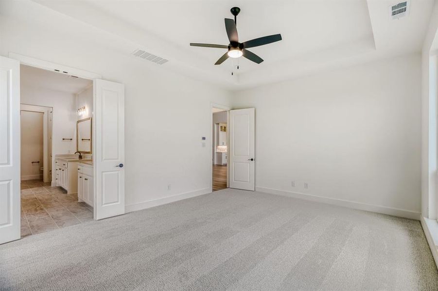 Unfurnished bedroom featuring light carpet, a ceiling fan, ensuite bath, and a tray ceiling
