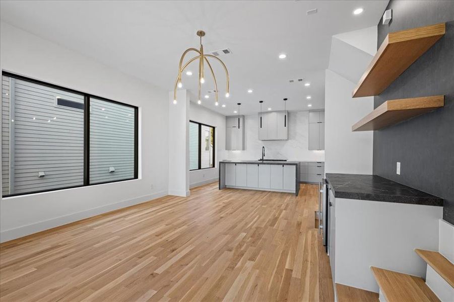 Dining area featuring open shelves, dark countertops, white cabinetry, hanging light fixtures, and light wood finished floors and staircase. Dining area featuring open shelves, dark countertops, white cabinetry, hanging light fixtures, and light wood finished floors and staircase.