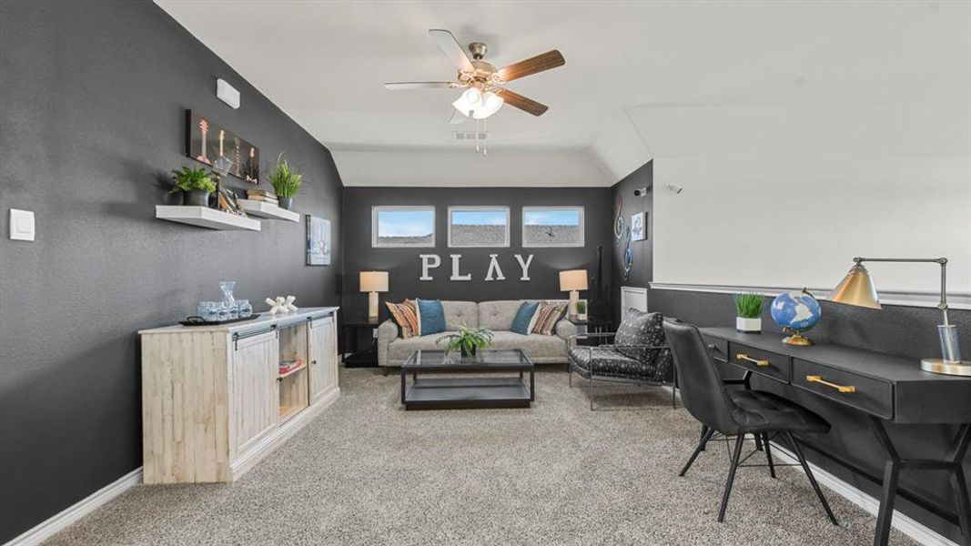 Carpeted loft area featuring a ceiling fan, three windows, and a built-in half-wall desk
