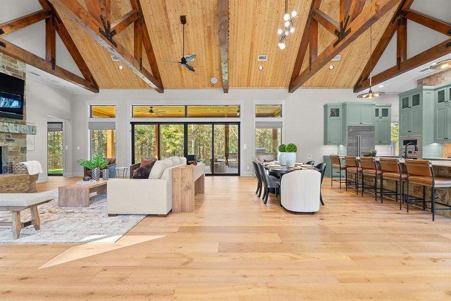 Living area featuring high vaulted ceiling, beamed ceiling, plenty of natural light, light wood finished floors, and a stone fireplace