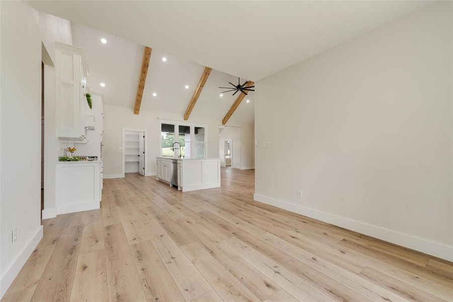 Spacious open-concept living area featuring light wood-finish flooring, vaulted ceilings with exposed wood beams, and recessed lighting