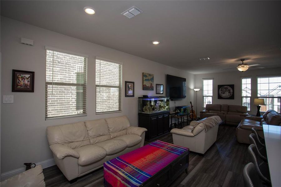 Living room with a ceiling fan, dark wood-style floors, visible vents, baseboards, and recessed lighting