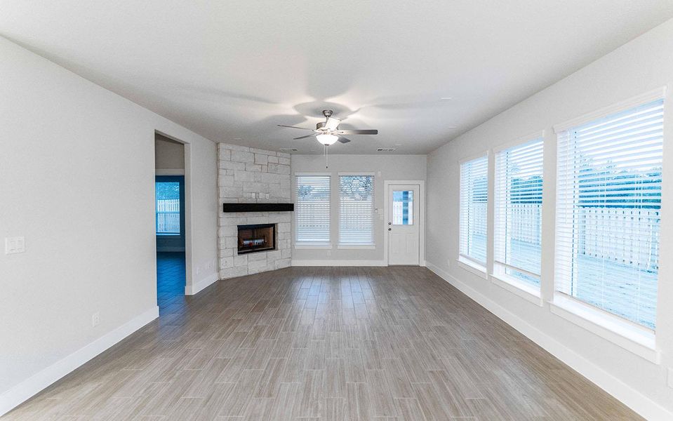 Unfurnished living room featuring a ceiling fan, a stone fireplace, baseboards, and wood finished floors