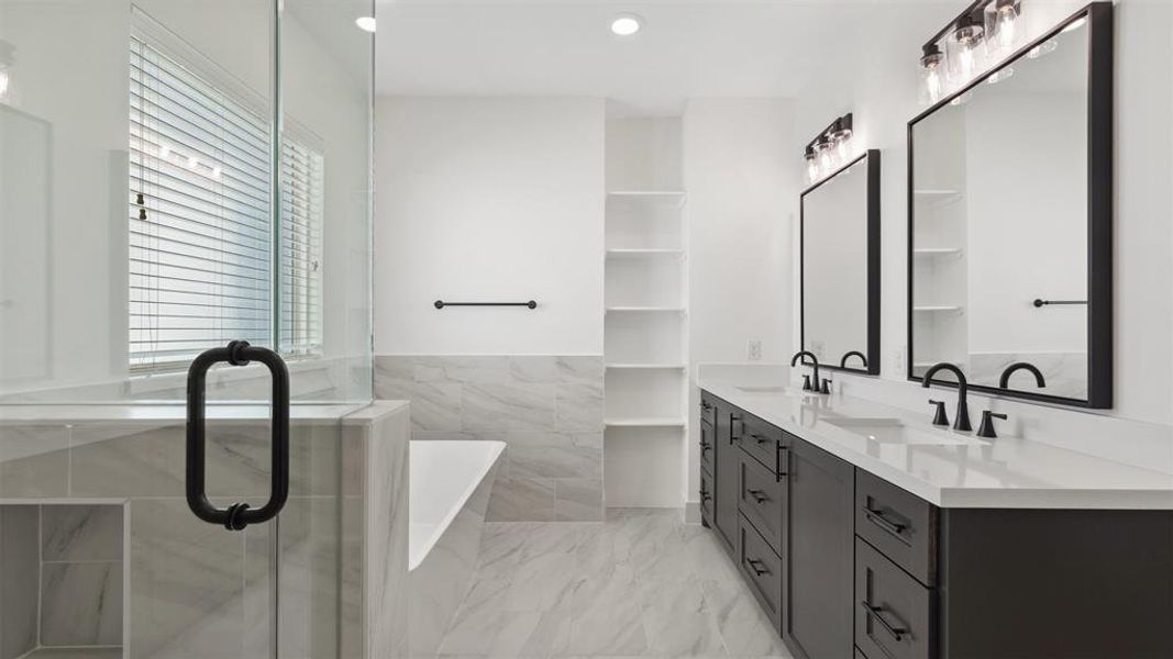 This modern bathroom features a spacious layout with a glass-enclosed shower, a separate bathtub, dual sinks with sleek black fixtures, ample storage, and contemporary lighting. The neutral color palette and elegant finishes create a luxurious feel.