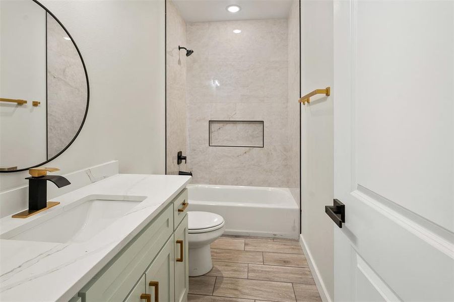 Bathroom featuring a white bathtub, light-toned tiled shower surround with an integrated niche, and wood-finish flooring Bathroom featuring a white bathtub, light-toned tiled shower surround with an integrated niche, and wood-finish flooring