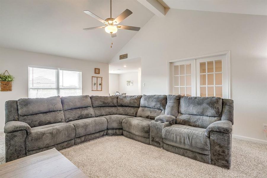Carpeted living area with high vaulted ceiling, beam ceiling, and ceiling fan