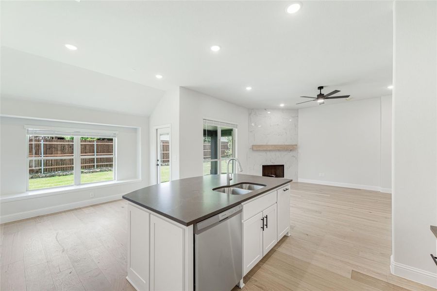 Kitchen island with dark countertop and sink open to living room with marble fireplace and light wood floors