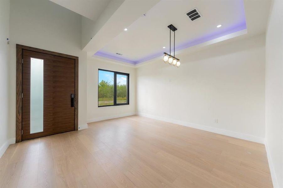 Living room featuring a raised ceiling, light wood-style flooring, and recessed lighting