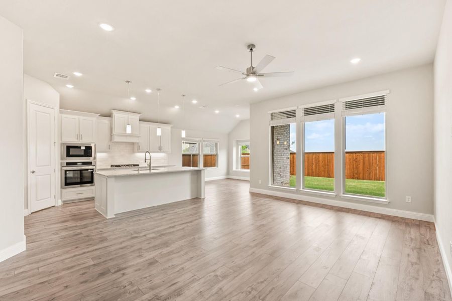Open-concept living area and kitchen with white cabinets, center island, hardwood floors, and large windows overlooking backyard Open-concept living area and kitchen with white cabinets, center island, hardwood floors, and large windows overlooking backyard