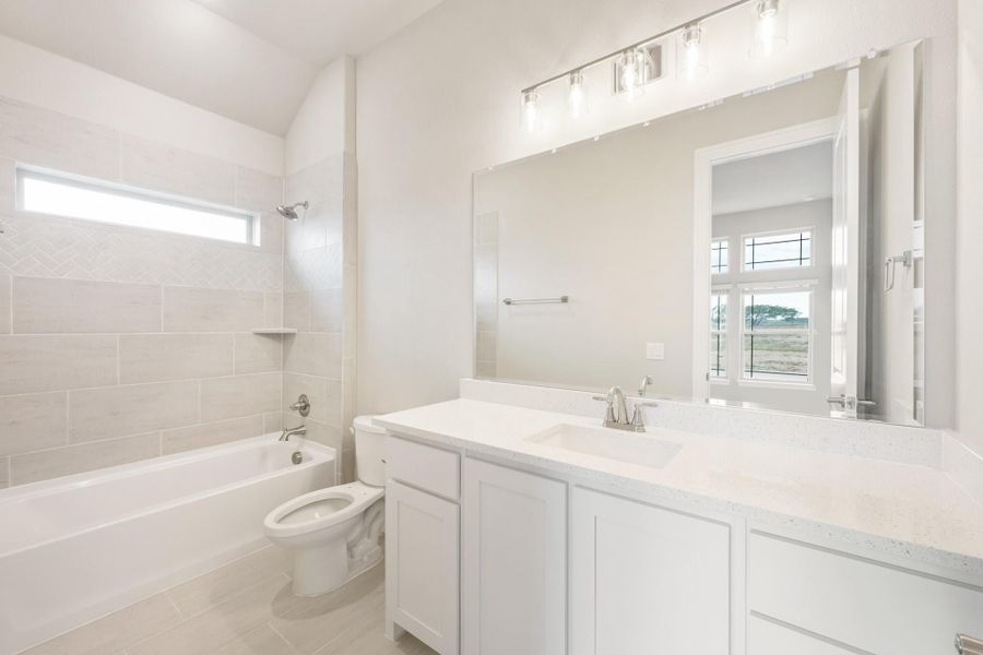 Bathroom with white double vanity, quartz countertop, tiled tub-shower combo, and large mirror with light bar above.