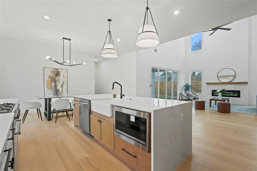 Kitchen featuring pendant lighting, stainless steel appliances, a glass covered fireplace, light wood-style floors, and a high ceiling