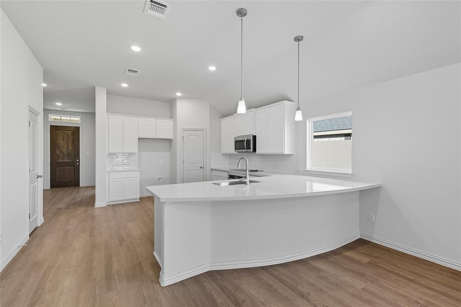 Kitchen featuring white cabinetry, light wood-type flooring, a peninsula, decorative light fixtures, and recessed lighting Kitchen featuring white cabinetry, light wood-type flooring, a peninsula, decorative light fixtures, and recessed lighting