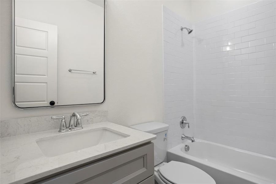 Full bathroom featuring vanity, tiled shower / bath combo, and toilet