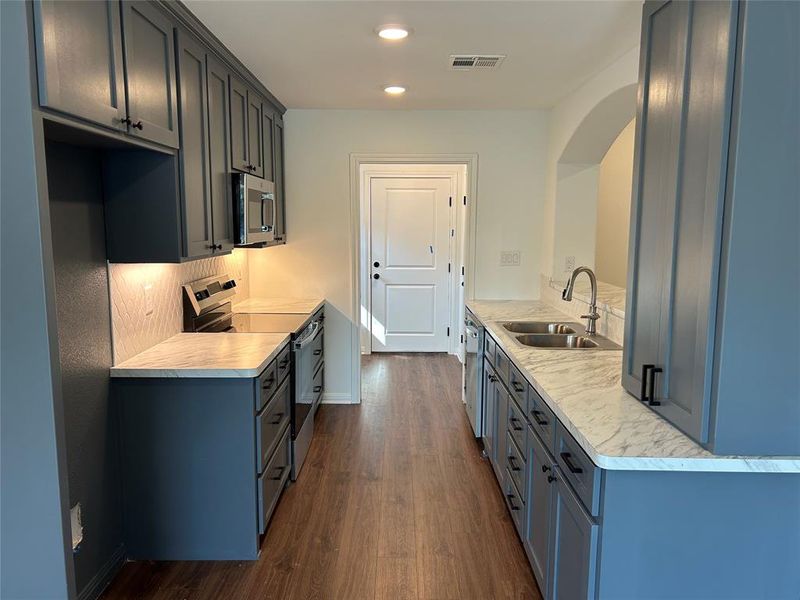 Kitchen with stainless steel appliances, light countertops, dark wood-style flooring, and recessed lighting