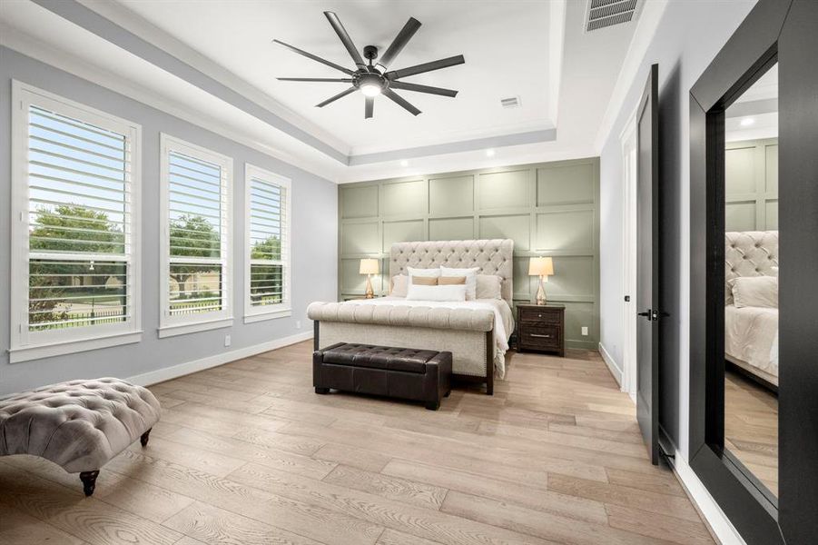 Large primary retreat highlighting accent wall, hardwood floors, tray ceiling with crown molding and accent lighting