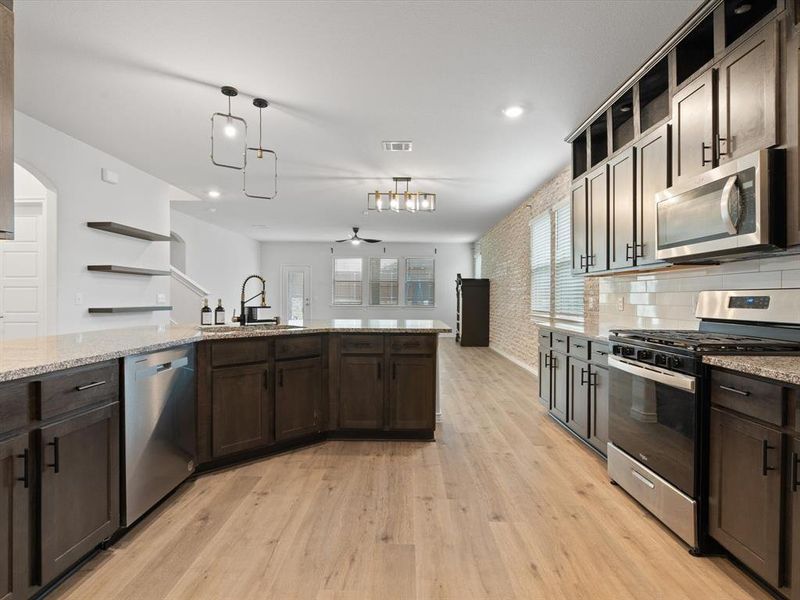 Kitchen featuring sink, light stone counters, light wood-type flooring, pendant lighting, and stainless steel appliances