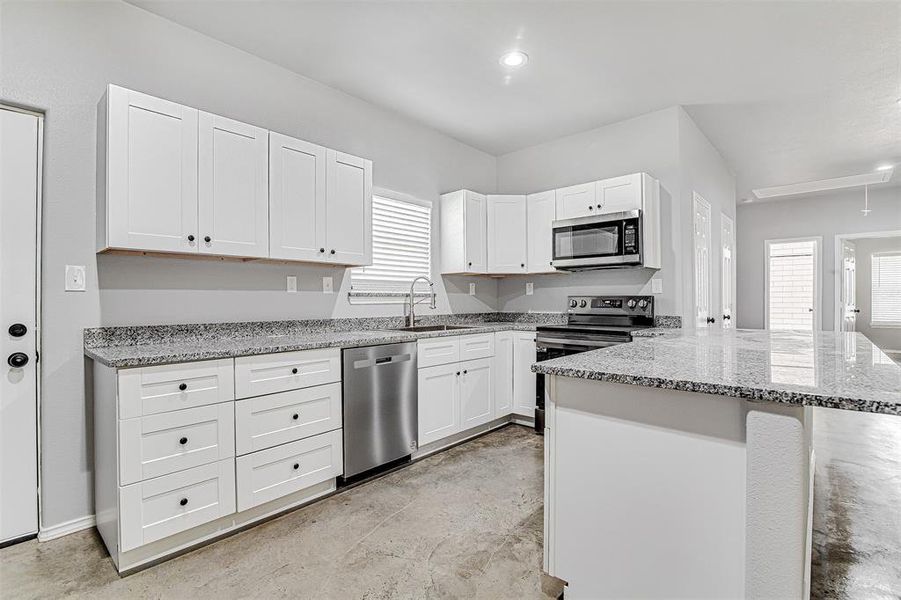 Kitchen with appliances with stainless steel finishes, a wealth of natural light, white cabinets, and sink