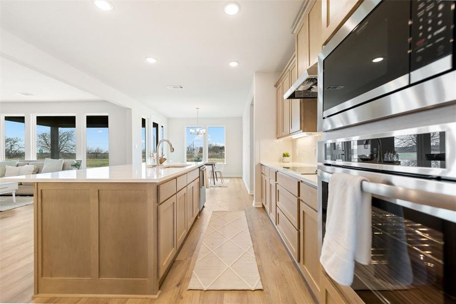 Kitchen featuring appliances with stainless steel finishes, light wood finished floors, recessed lighting, light brown cabinetry, and a kitchen island with sink