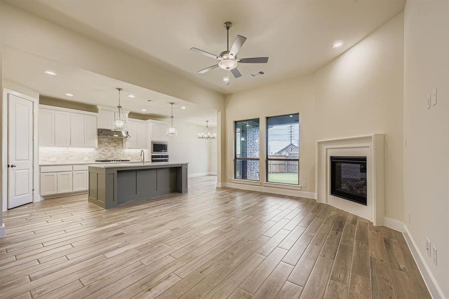 Kitchen featuring open floor plan, white cabinets, an island with sink, tasteful backsplash, and decorative light fixtures