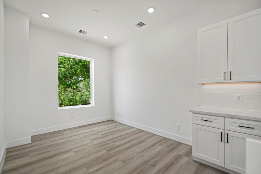 The dining area is bright and airy with LVP flooring, recessed lighting, and a large window offering a view of greenery. Features white soft closing cabinetry and a sleek quartz countertop, creating a clean and modern look.