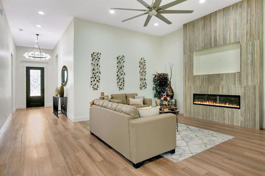 Spacious living area featuring high ceilings, wood-finish flooring, recessed lighting, and a modern linear fireplace with a textured accent wall Spacious living area featuring high ceilings, wood-finish flooring, recessed lighting, and a modern linear fireplace with a textured accent wall