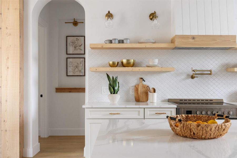 Kitchen featuring a white scalloped tile backsplash, open wood shelving, stainless steel range, and a brass pot filler