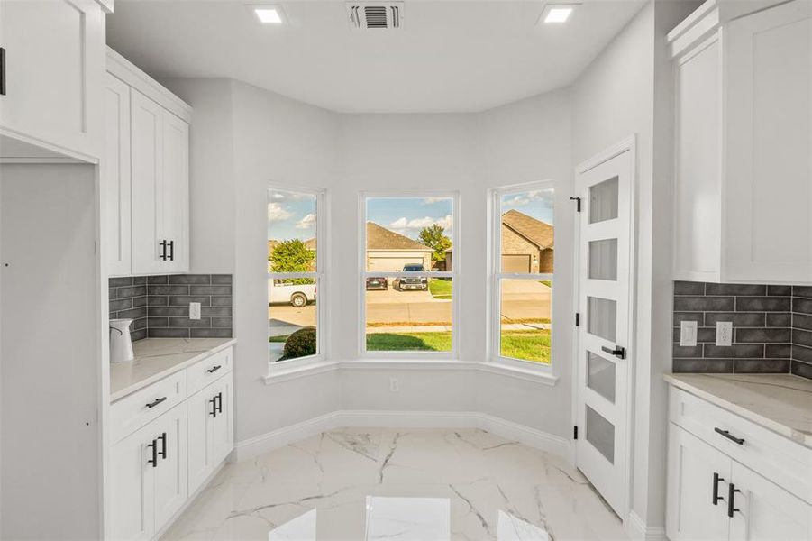 Kitchen with tasteful backsplash, light stone counters, white cabinets, and recessed lighting
