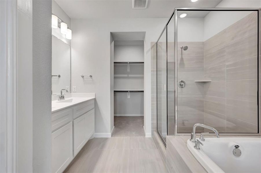 Bathroom featuring a dual vanity with white cabinetry and a large mirror, a glass-enclosed shower with tiled walls and a built-in niche, a soaking tub with chrome fixtures, and a walk-in closet with built-in shelving