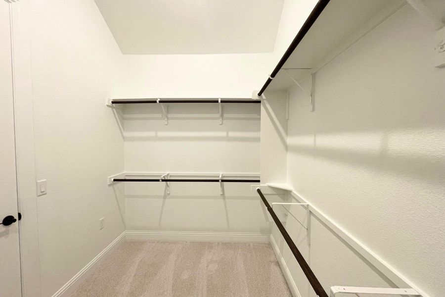 Custom built-in shelving and hanging rods maximize storage within this carpeted walk-in closet. Custom built-in shelving and hanging rods maximize storage within this carpeted walk-in closet.