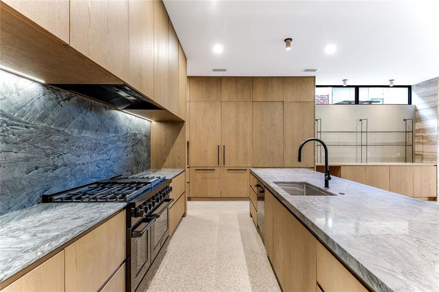 Kitchen featuring Wakanda quartzite countertops and backsplash, custom modern cabinets, exposed aggregate flooring, an island with sink, and recessed lighting.