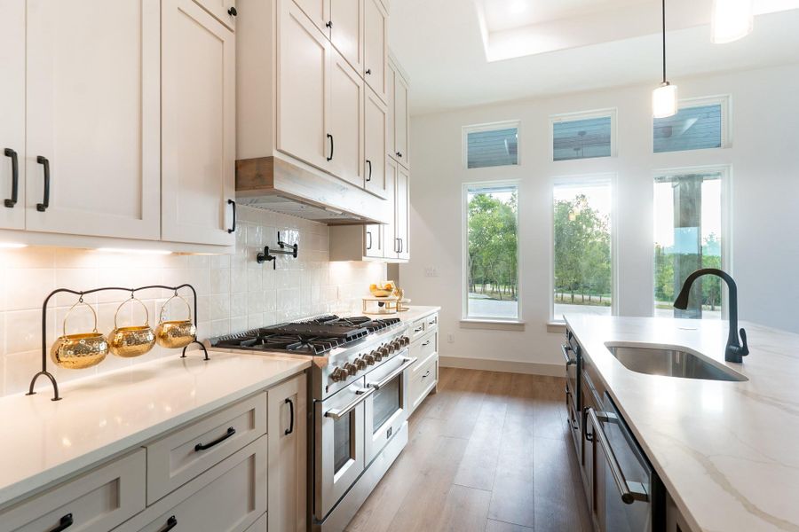 Kitchen featuring range with two ovens, light wood-type flooring, hanging light fixtures, decorative backsplash, and light stone counters Kitchen featuring range with two ovens, light wood-type flooring, hanging light fixtures, decorative backsplash, and light stone counters