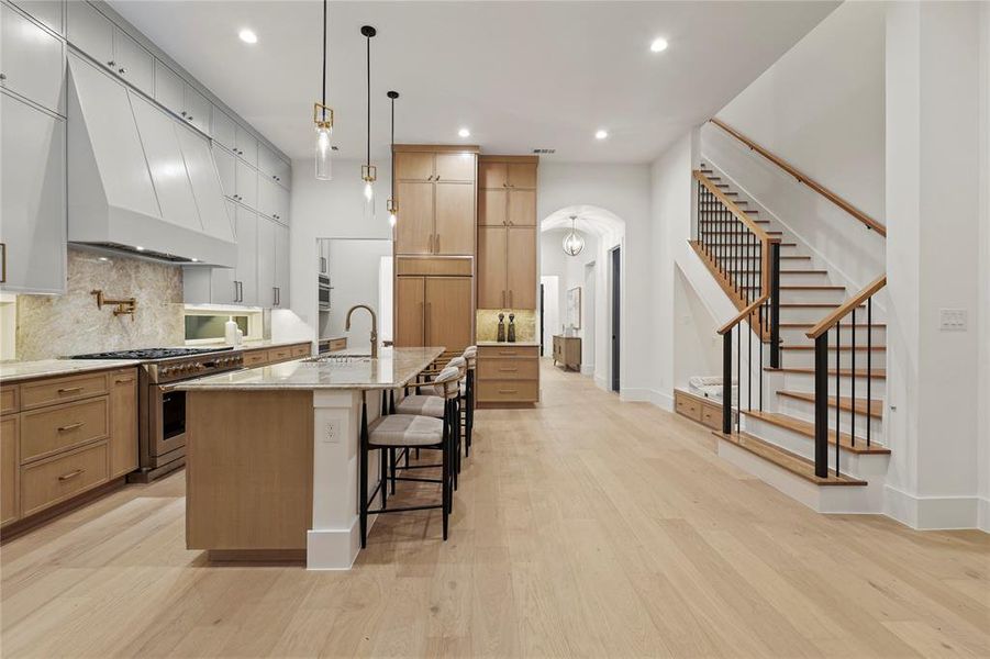 Kitchen with a breakfast bar, custom range hood, tasteful backsplash, light stone counters, and high end stainless steel range oven