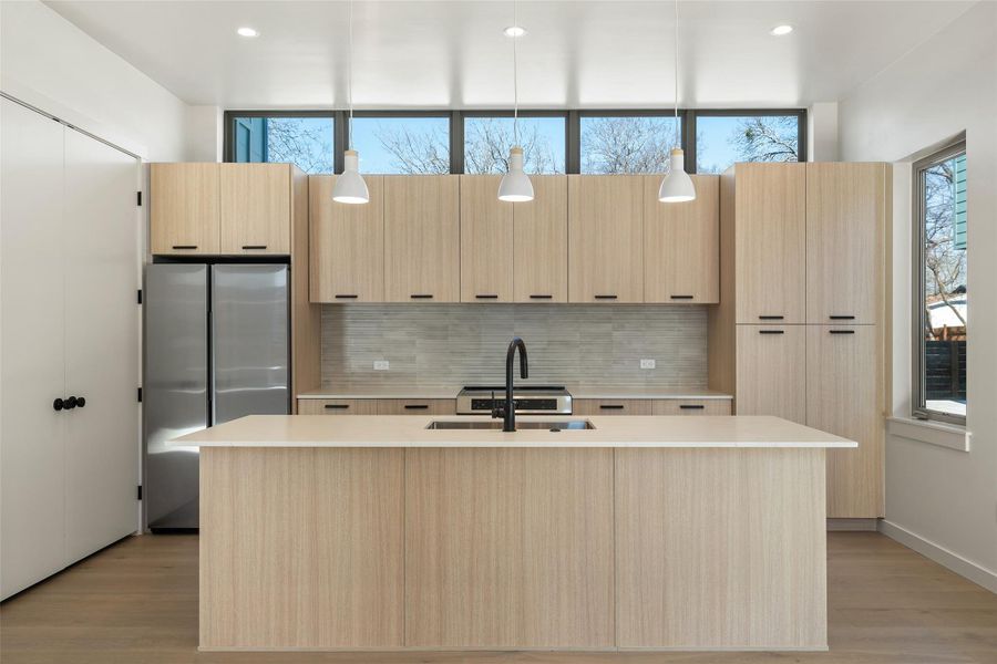 Kitchen with tasteful backsplash, freestanding refrigerator, light countertops, light brown cabinets, and a sink