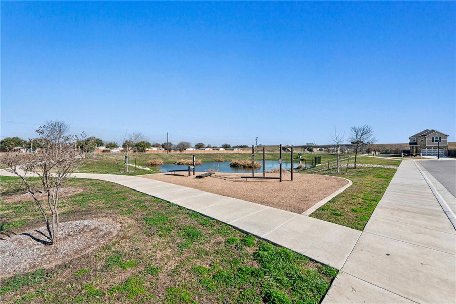 Enjoy a serene view of the community’s exercise area, overlooking a tranquil pond and surrounded by scenic walking trails perfect for biking, walking, running, and dog-walking. Sidewalks and a grassy knoll provide additional space for outdoor activities, creating an inviting and versatile setting for an active lifestyle.