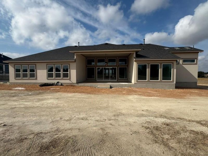 Rear view of house with a patio area, roof with shingles, and stucco siding