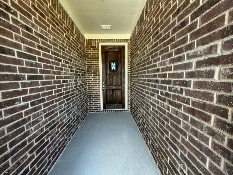 Inviting entryway featuring a rich brick facade, a robust wood entry door with decorative glass inlay, and a smooth concrete floor