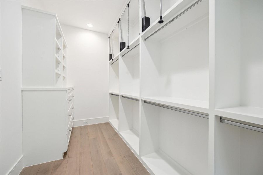 Spacious primary closet features built-in storage and ample room for hanging clothes with pull-down bars for accessing all custom storage solutions. Spacious primary closet features built-in storage and ample room for hanging clothes with pull-down bars for accessing all custom storage solutions.