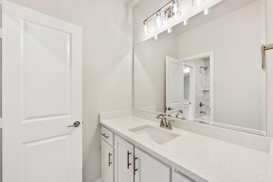 Bathroom vanity with white cabinets, quartz countertop, single sink, and large mirror with overhead lighting