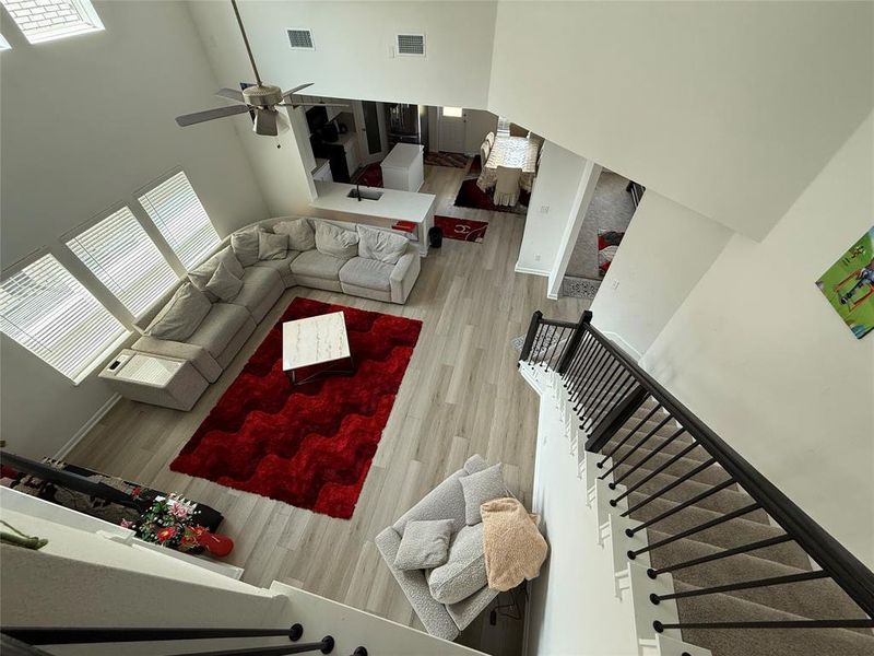 Vaulted ceiling great room with wood-finish flooring, a contemporary ceiling fan, and multiple windows with blinds
