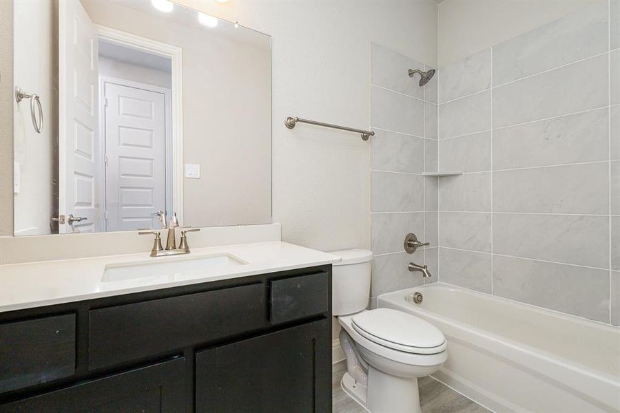 Full bathroom with vanity, wood-type flooring, tiled shower / bath combo, and toilet