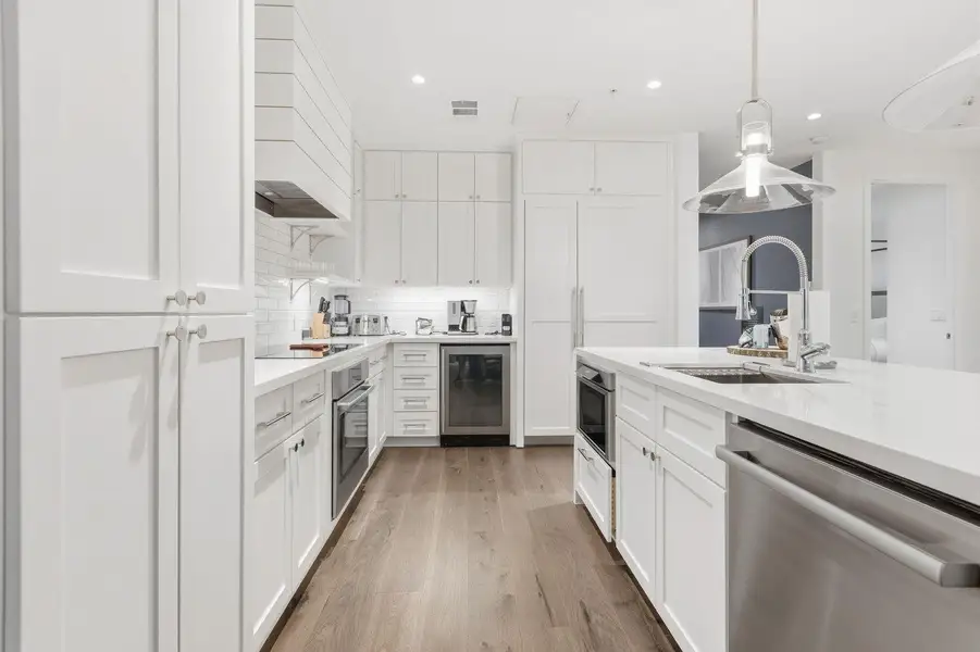Kitchen with stainless steel appliances, white cabinetry, beverage cooler, tasteful backsplash, and light wood-type flooring