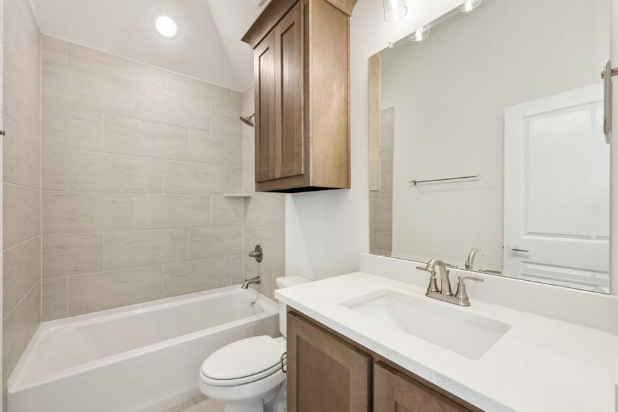 Bathroom with tiled tub surround, white quartz vanity, wood cabinets, and vaulted ceiling
